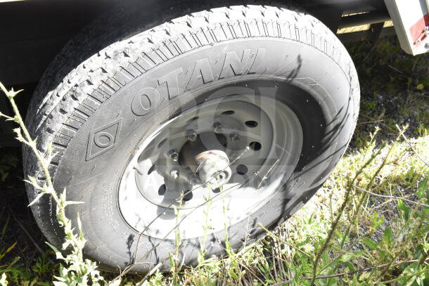 Rock Solid Cargo trailer wheel with OTANI tire. Visible plants around wheel. Part of a 28' food trailer shell.