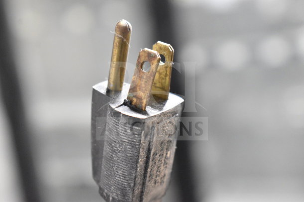 Close-up image of a three-prong electrical plug, showing details of metal prongs and surface wear.