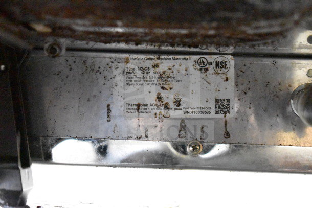 Thermoplan Mastrena M2-CS espresso machine tag, details voltage 208V, model number, serial number 410038865, and production date.