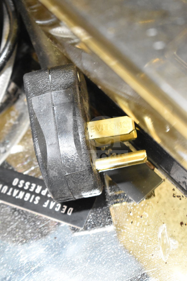 Thermoplan Mastrena M2-CS espresso machine power plug detail, showing metal prongs and brand marking on a metallic surface.