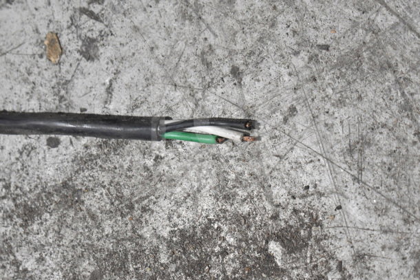 A damaged power cable with exposed wires on a rough, scratched surface.