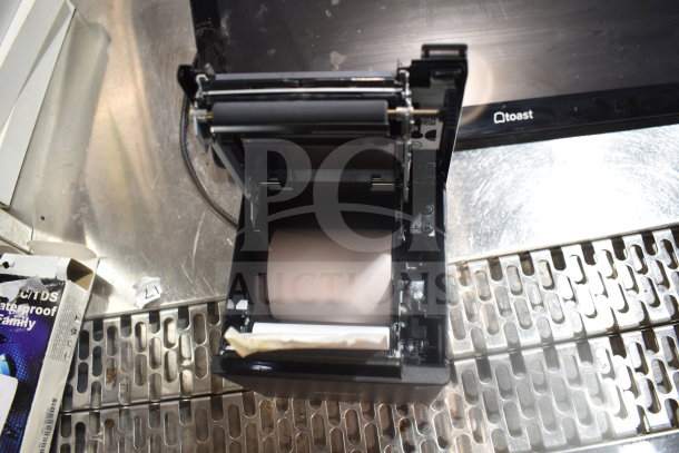 POS monitor and open Bixolon SRP-S300 receipt printer on a metal surface, showing interior paper roll and mechanics.