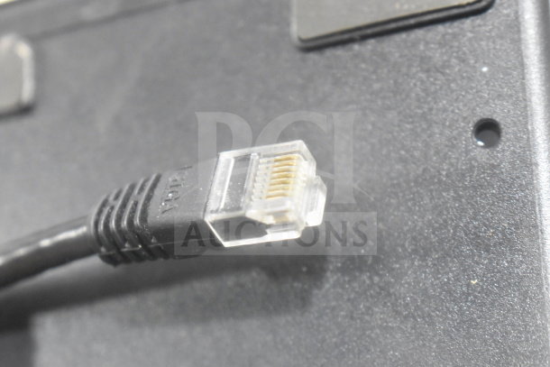 Close-up of an Ethernet cable connector on a surface, part of an auction lot including a POS monitor and receipt printers.