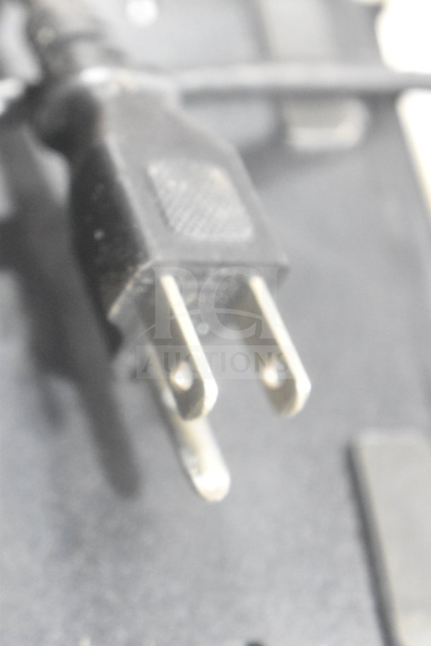 Blurred image of a standard two-prong power plug, part of auction lot with POS monitor and printers.