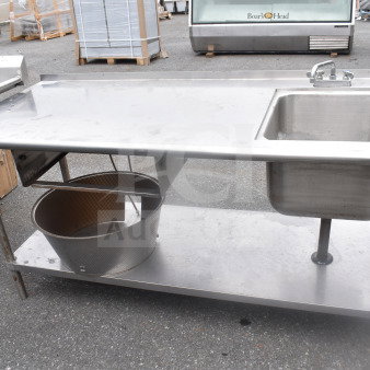 Commercial stainless steel table with sink bay, faucet, and durable under shelf. Used condition with visible wear.