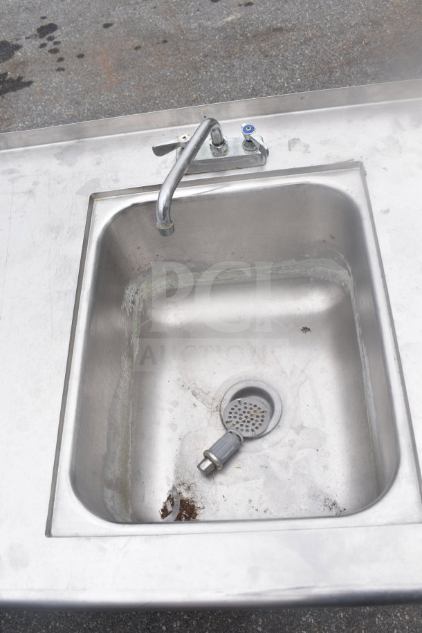 Commercial steel table with integrated sink bay, single faucet, under shelf, and visible wear. Ideal for industrial use.
