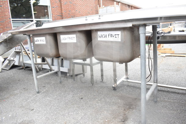 Commercial 3-bay sink with dual drain boards, stainless steel, labels for washing kale and fruit, outdoor setting.