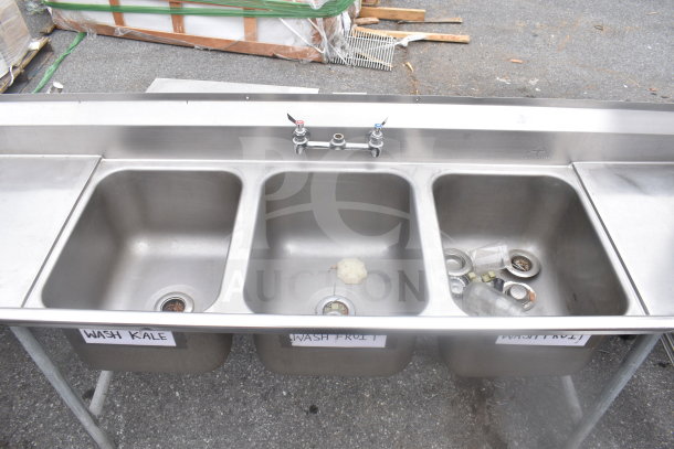Commercial 3-bay sink with dual drain boards, stainless steel, includes faucets, visible labels indicate washing instructions.