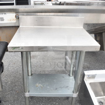 Regency commercial table with backsplash and under shelf, stainless steel, visible wear on lower shelf, sturdy legs.