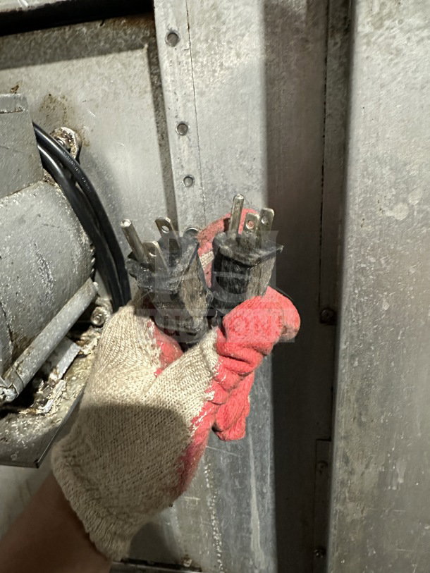 A gloved hand holds two pronged plugs near industrial equipment, highlighting the electrical connections.