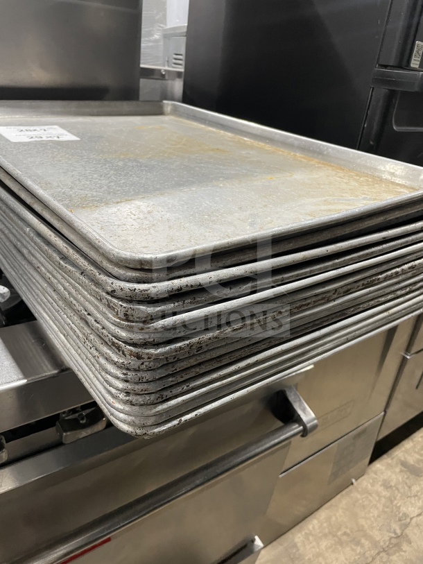 Stack of commercial aluminum full-size baking sheet pans in used condition, showing wear. Auction for 7x sheets.