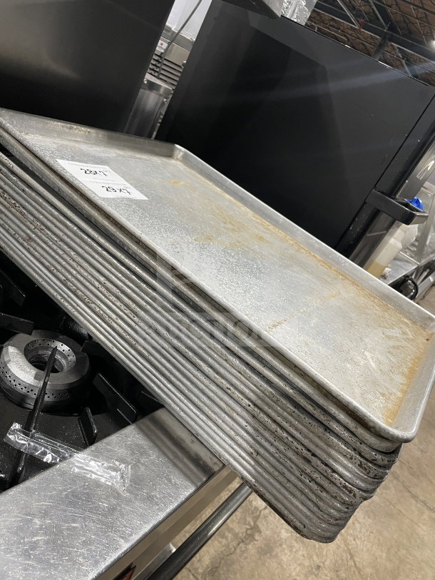 Stack of commercial aluminum full-size baking sheet pans, slightly worn. Labels indicate dimensions: 28" x 16".