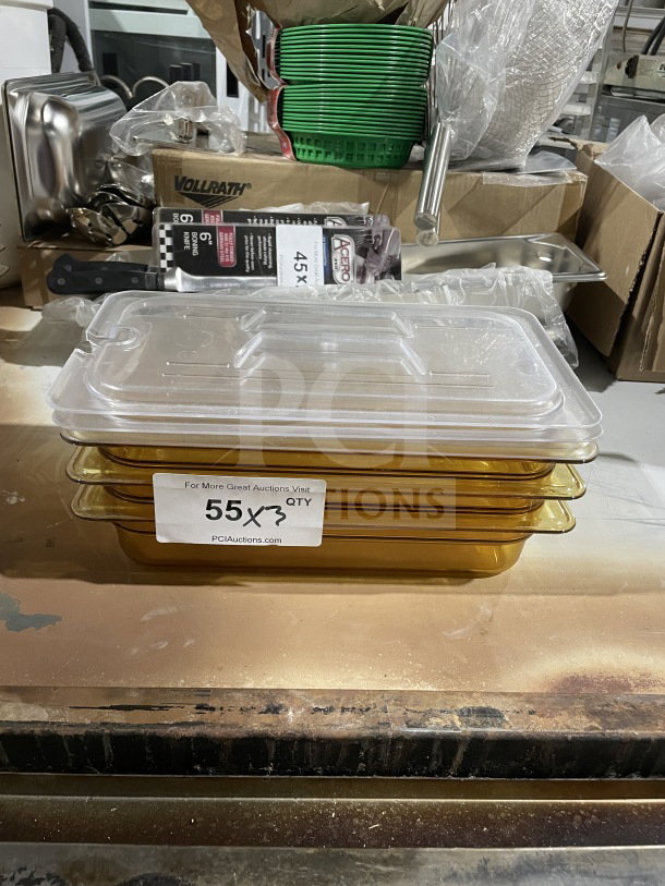 Clear stack of amber food storage pans with lids, labeled "55 QTY." New condition. Other kitchenware visible in background.