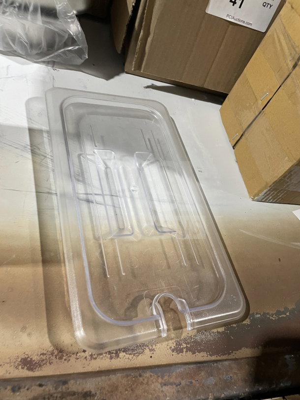 Clear plastic lid, brand new, rectangular with lift tab. On metal surface, boxes nearby. Perfect for storage or cooking.