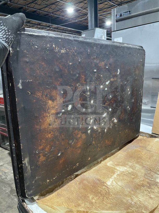 Commercial aluminum full-size baking sheet pan, heavily used with visible wear and patina, resting on a wooden surface.