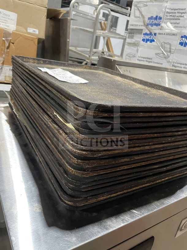 Stack of commercial aluminum full-size baking sheet pans. Visible wear, suitable for heavy-duty kitchen use.