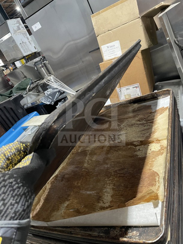 Commercial aluminum full-size baking sheet pan in used condition, stacked, with visible wear and parchment paper lining.