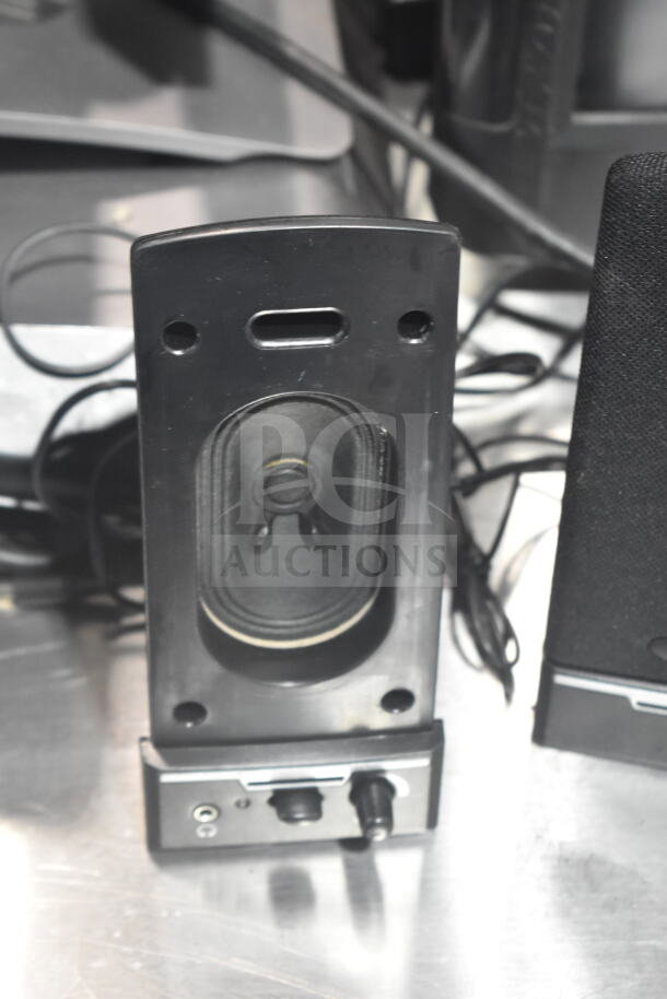 Close-up of a speaker from a POS system, showing front grille and control knobs. Speaker is in used condition.