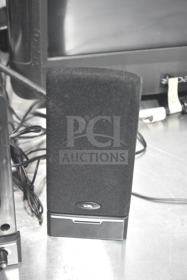 POS system with two monitors, visible black speaker in good condition, cables attached on metallic surface.