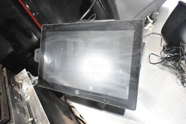 POS system with HP monitor, showing a slightly worn screen, cables, and a black speaker, on a metal surface.