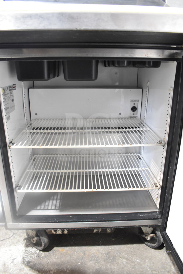 True TSSU-27-12M-B commercial sandwich salad prep table with two-tier over shelf. Features steel wire shelves, caster wheels, and a Bain Marie top. Model and electrical specs label visible inside.