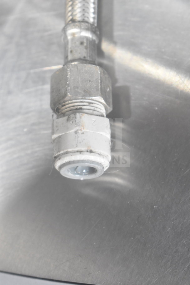 Braided metal hose, possibly part of Schaerer Coffee Art Espresso Machine, against a metal surface.