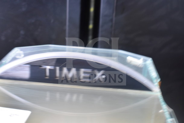 Clear acrylic display rack with "TIMEX" branding, featuring a curved design and reflective surface. Suitable for showcasing items.