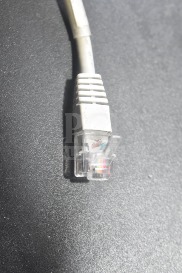 Close-up of an Ethernet cable connector on a black surface, part of an auction lot including cash drawers and Epson printers.