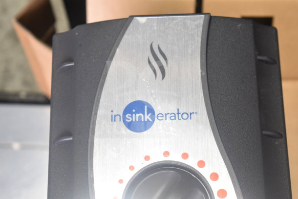 Two Insinkerator hot water heaters in good condition, featuring a stainless steel panel with logo branding, available for auction.