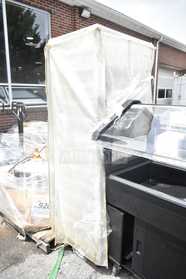 Commercial pan transport rack on commercial casters with cover, used condition, situated outdoors on concrete surface.