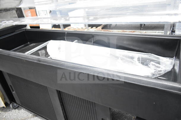 Cambro black poly salad bar with multiple compartments, durable material, on wheels, covered in plastic wrap, in good condition.
