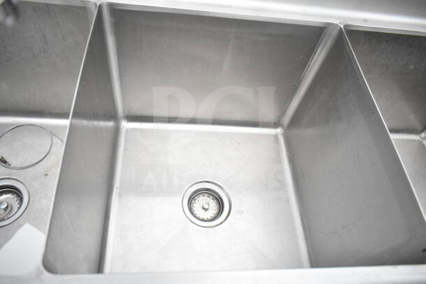 Commercial 3 bay sink with faucet and handles. Stainless steel, clean, with visible sink drains in each compartment.