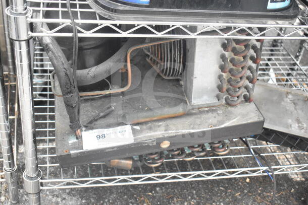 Embraco FFI 12HBX compressor, 220 volts, used condition, visible wear and rust marks, on wire shelving.