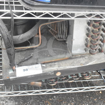 Embraco FFI 12HBX compressor, 220 volts, used condition, visible wear and rust marks, on wire shelving.