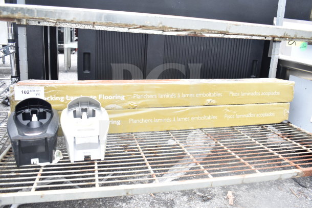 Four items include black and white soap dispensers and two boxes of laminate flooring with packaging text. Items on metal rack.