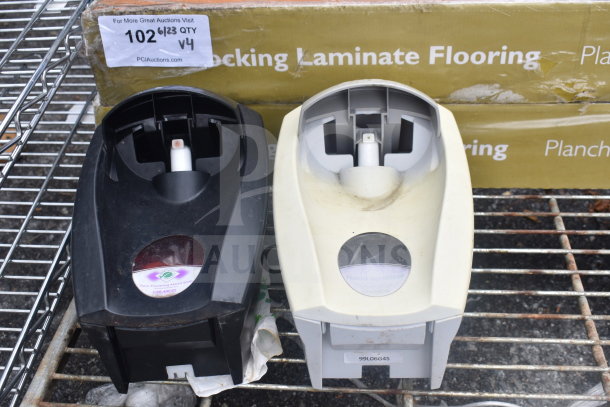 Two wall-mounted soap dispensers, one black, one beige, with visible brand labels. Behind them, boxes of laminate flooring.