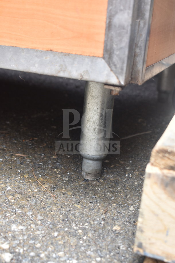 Close-up of a metal leg on a Duke SUBBD-60-LM Commercial Soda Station, showing slight wear, on an asphalt surface.