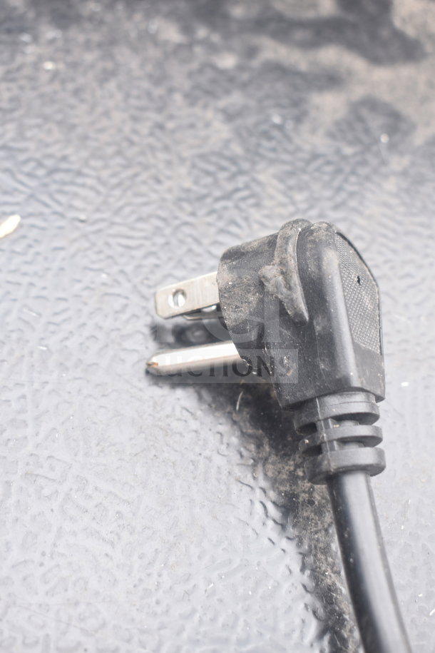 Alt text: Close-up of a dust-covered black power plug on textured surface.