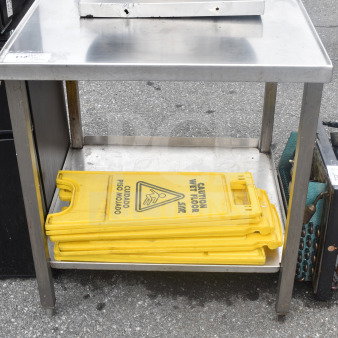 Stainless steel commercial table with under shelf, holds stacked yellow "Caution Wet Floor" signs, in good condition.