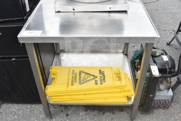 Commercial stainless steel table with under shelf, includes caution wet floor signs. Table has minor surface wear.
