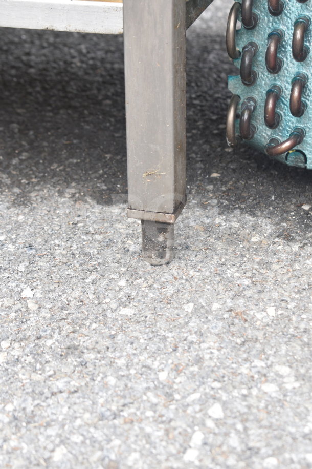 Commercial table leg close-up, showing metal construction and under shelf support, in used condition on asphalt.