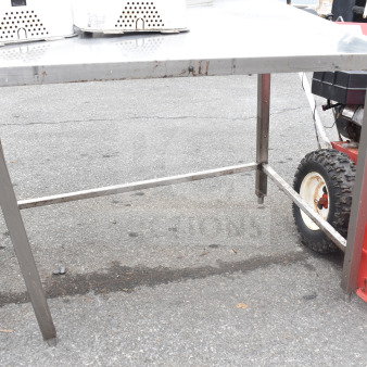 Metal table with a rectangular top and sturdy legs, used condition. Signs of wear and some rust visible on the frame.