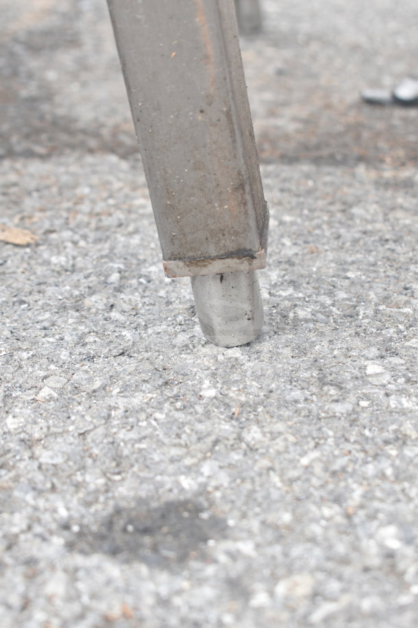 Close-up of metal table leg on concrete, showing wear and patina.