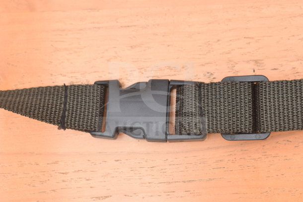 Close-up of a black plastic buckle on a dark woven strap, resting on a wooden surface.