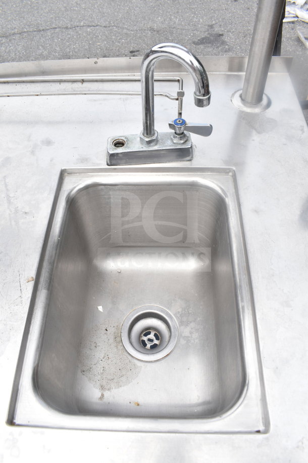 Commercial table with integrated sink bay, featuring faucet, over shelf, and under shelf. Stainless steel, lightly worn condition.