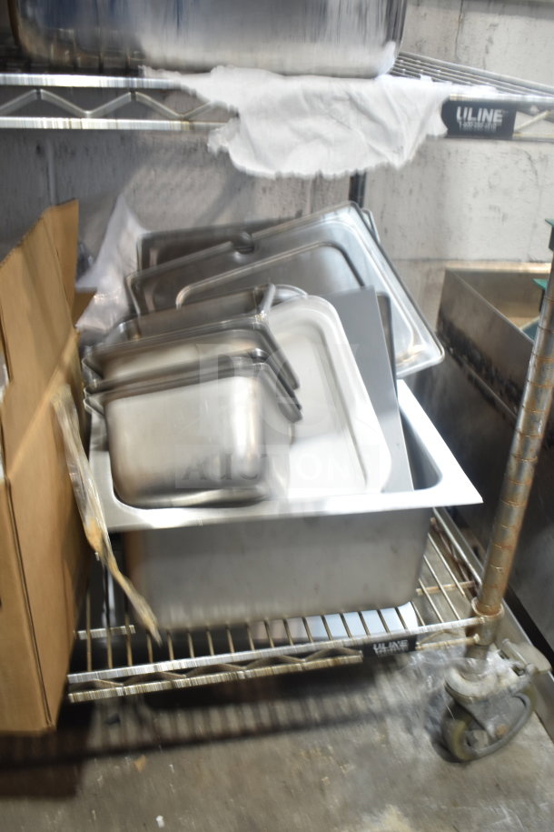 Tiered lot of stainless steel drop-in bins on a wire shelf, alongside cardboard boxes. Items appear in used condition.