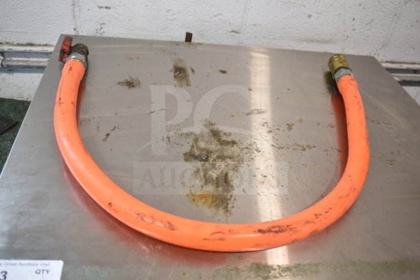 Orange gas hose with brass fittings on a metallic surface, showing signs of wear. Auction label visible.