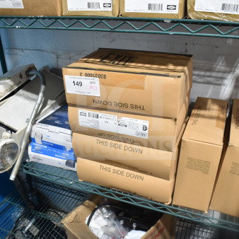 Boxes of assorted items including a DualLite exit sign and Cooper LED outdoor emergency light on a metal shelf. Auction lot 149.