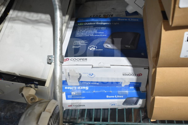 Boxes of Cooper Sure-Lites LED Outdoor Emergency Lights on a shelf. Packaging shows logo and "wet location" use.