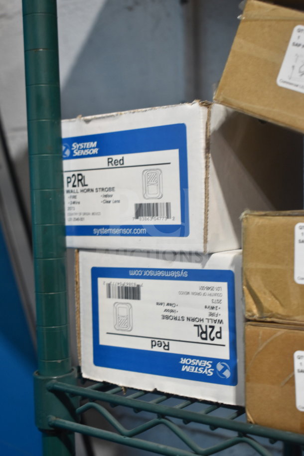 Boxes of System Sensor P2RL Red Wall Horn Strobe, new in packaging, stacked on a metal shelf.